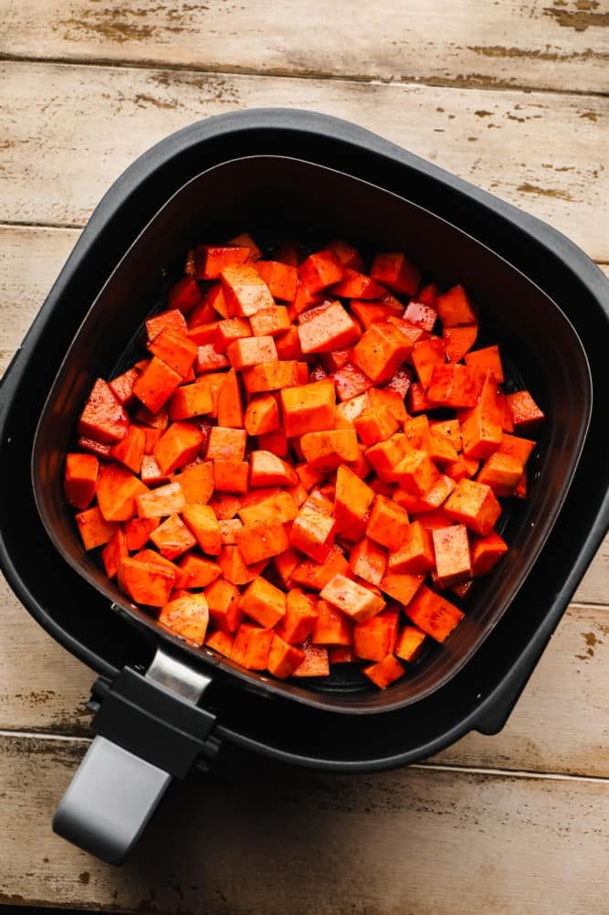 uncooked sweet potatoes chopped in an air fryer on wood background.