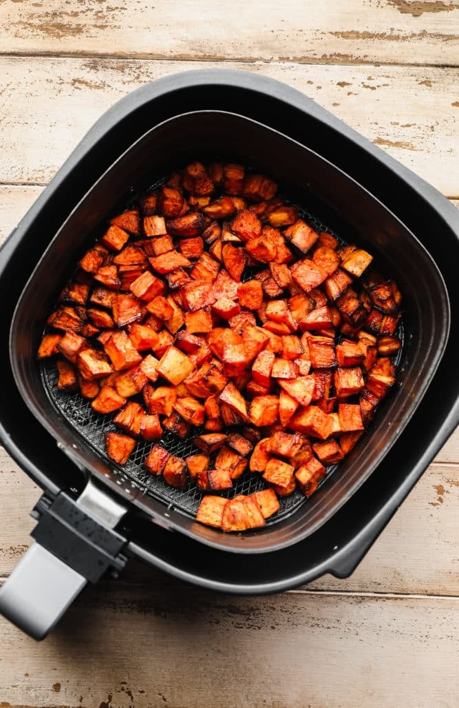 an air fryer with some cooked sweet potato chunks in it.