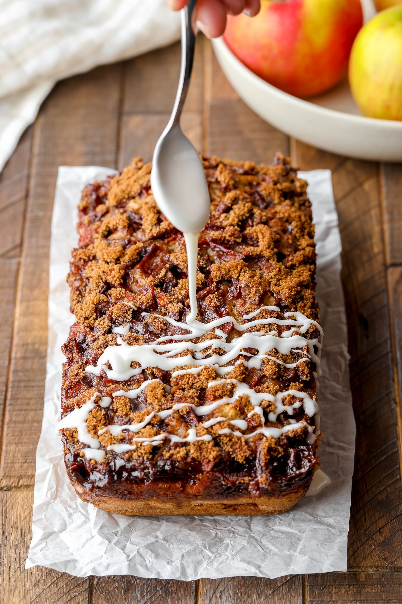 Drizzling a thin, white icing over a loaf of apple fritter bread.