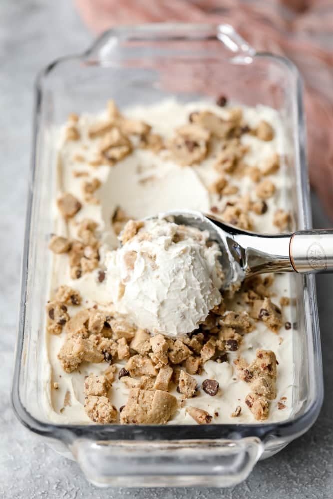 dairy free ice cream in a loaf glass dish with ice cream scooper, cookie dough in it.