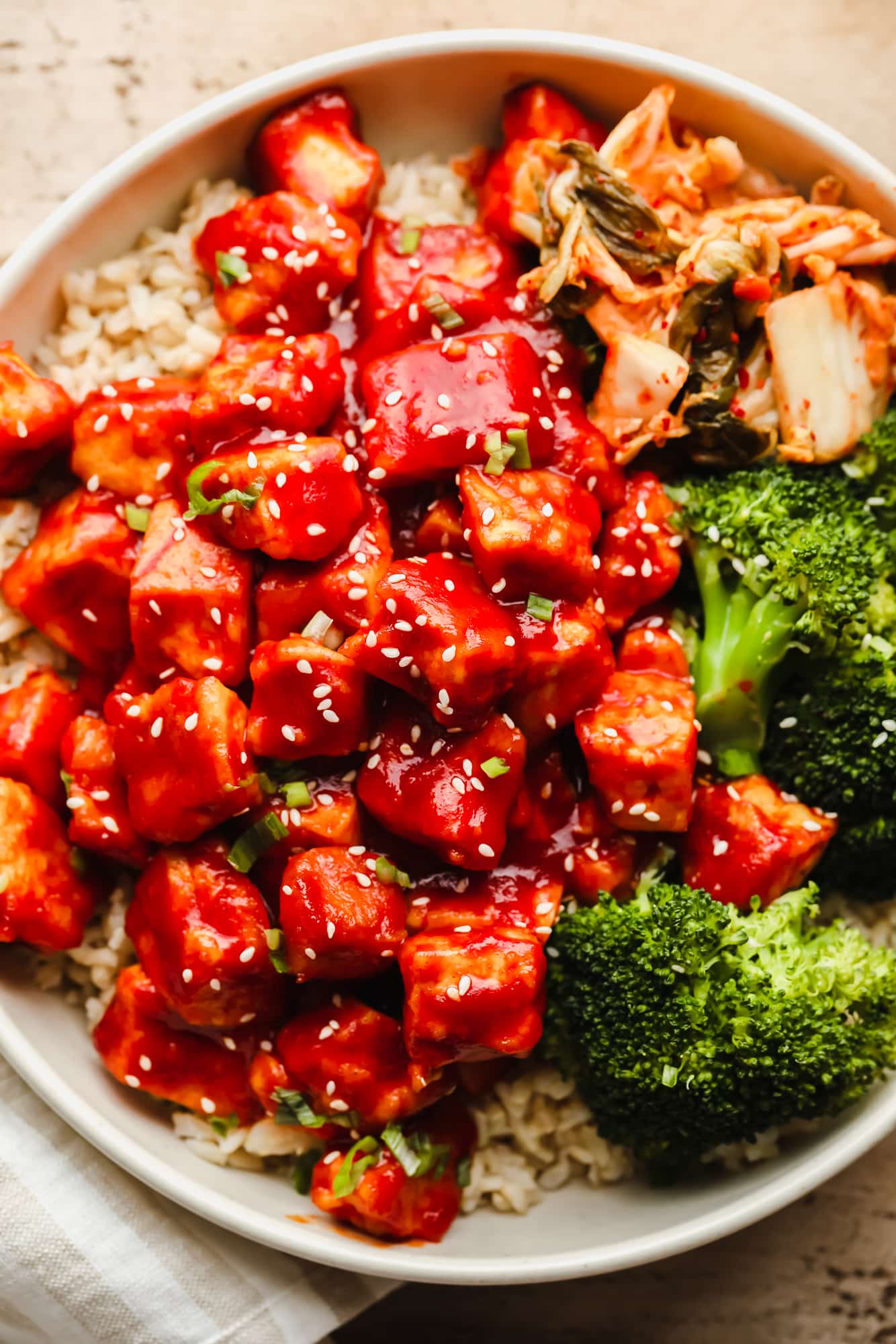 close up on Gochujang Tofu in a white bowl with rice, broccoli, and kimchi.