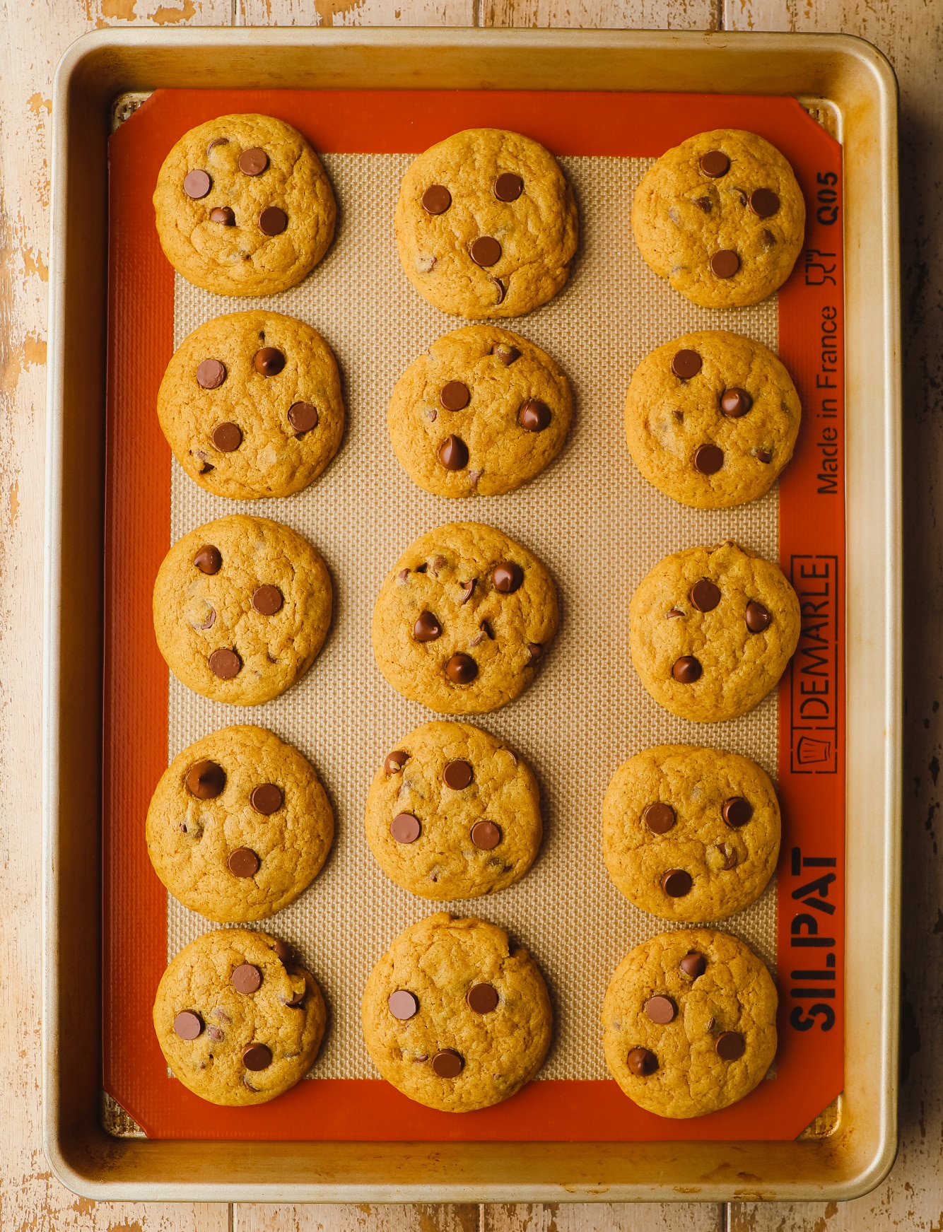 baked pumpkin chocolate chip cookies in rows on a baking sheet.