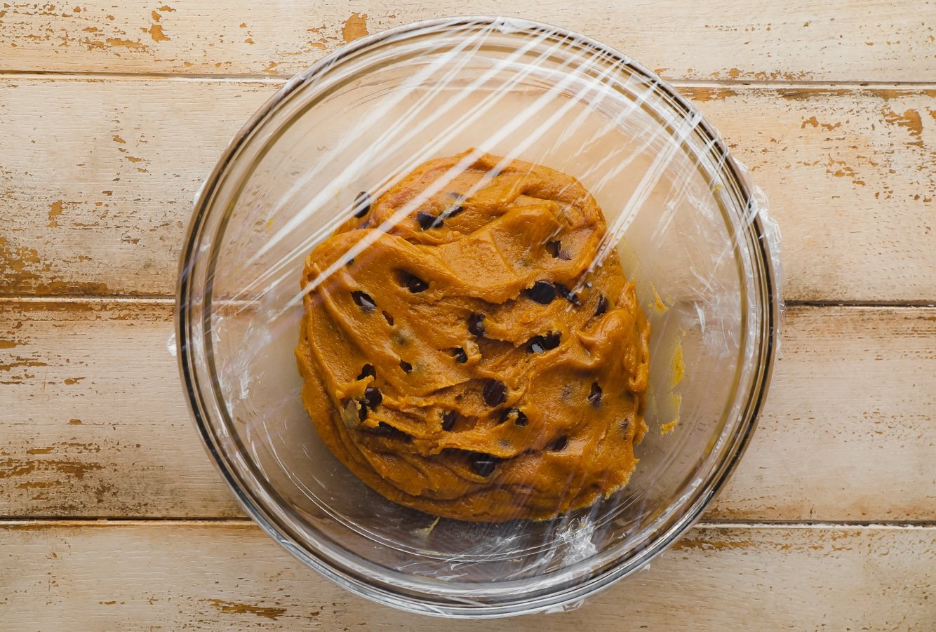 Pumpkin Chocolate Chip Cookie dough in a glass bowl covered with plastic wrap.