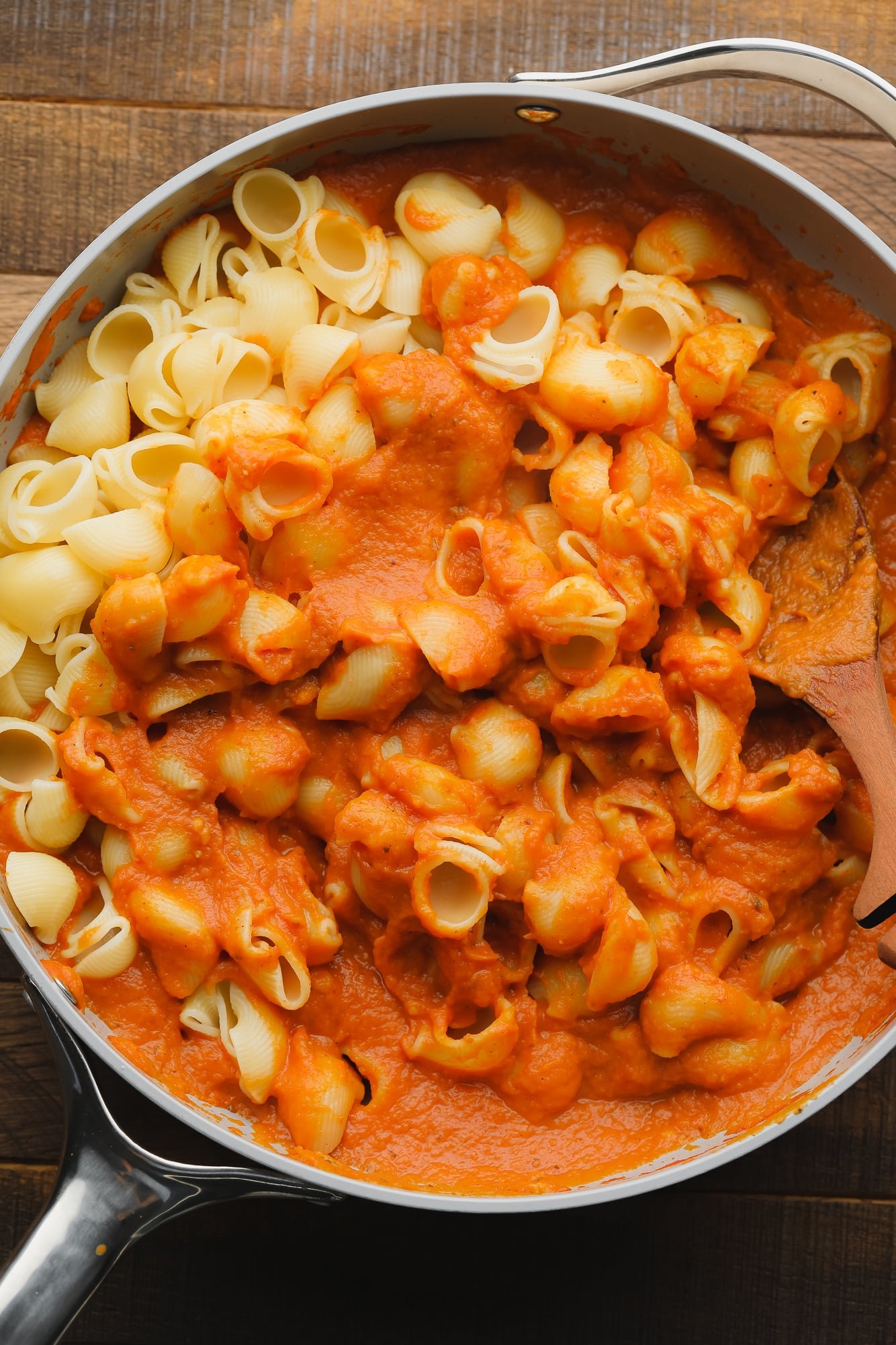 Stirring cooked pasta noodles into a skillet with pumpkin pasta sauce.