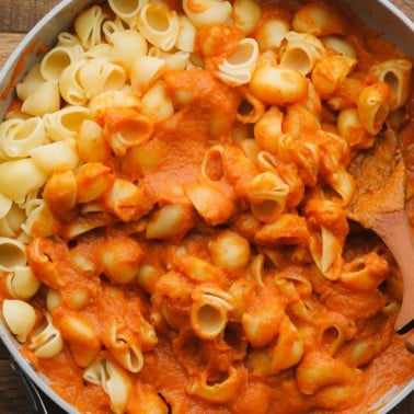 Stirring cooked pasta noodles into a skillet with pumpkin pasta sauce.