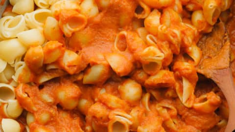 Stirring cooked pasta noodles into a skillet with pumpkin pasta sauce.