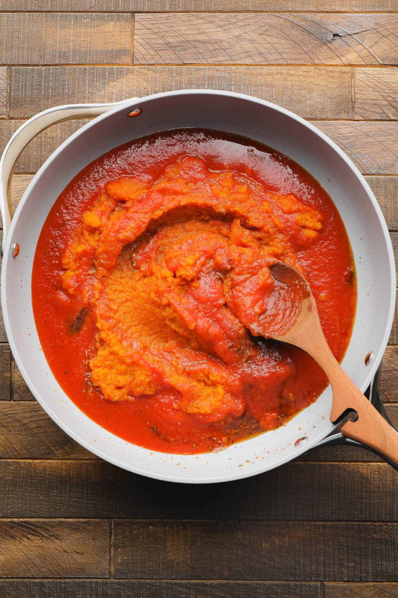 using a wooden spoon to stir pumpkin puree and tomato sauce together in a skillet.
