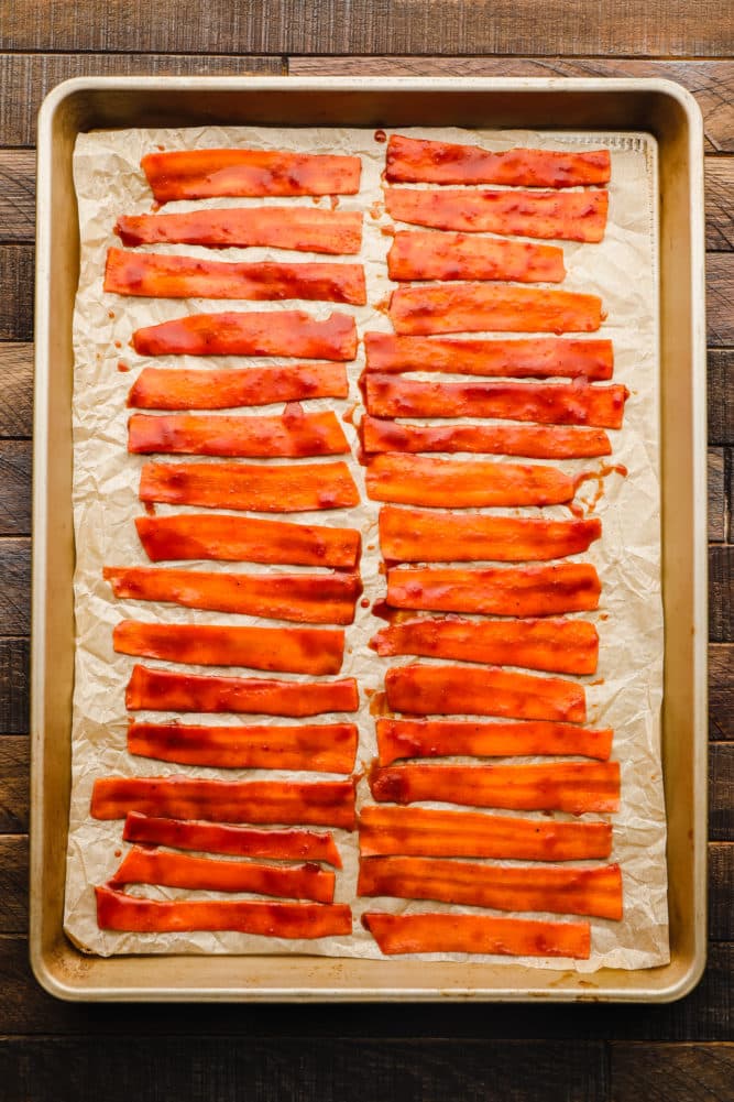 rows of marinated carrot strips on a parchment lined baking sheet.