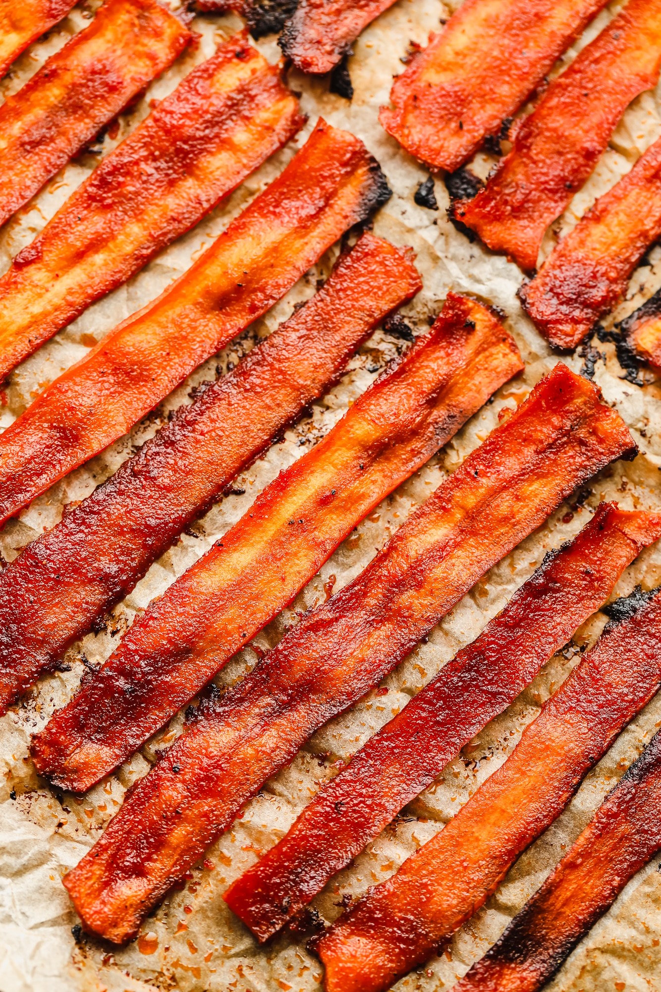 close up on strips of vegan bacon laying on a parchment-lined baking sheet.