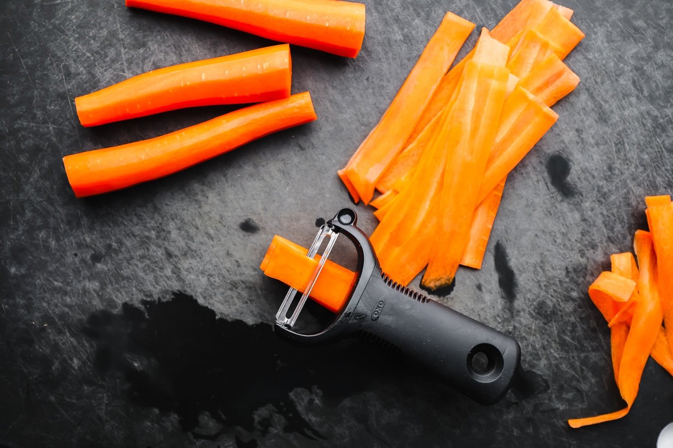 a black vegetable peeler peeling thin strips from a carrot.