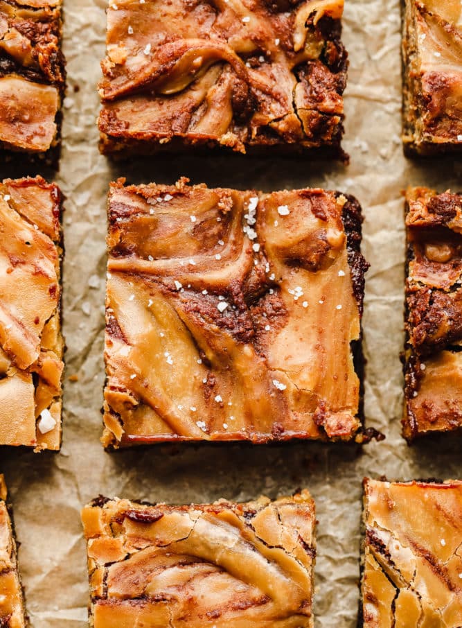 close up shot of caramel brownie with salt sprinkled on top, laying on parchment paper.