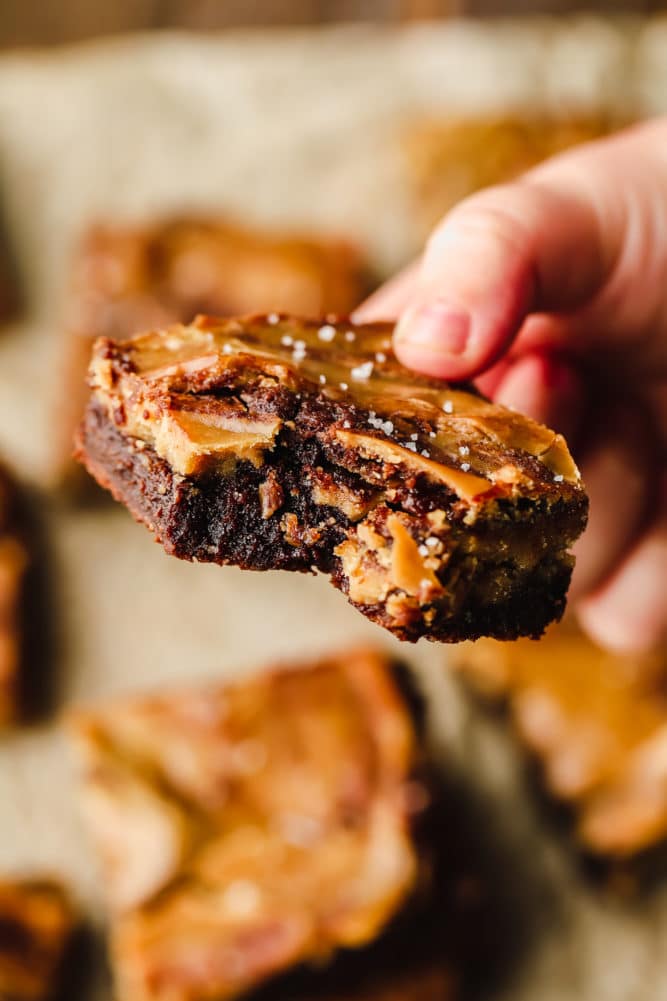 hand holding a brownie with caramel and a bite taken out of it.