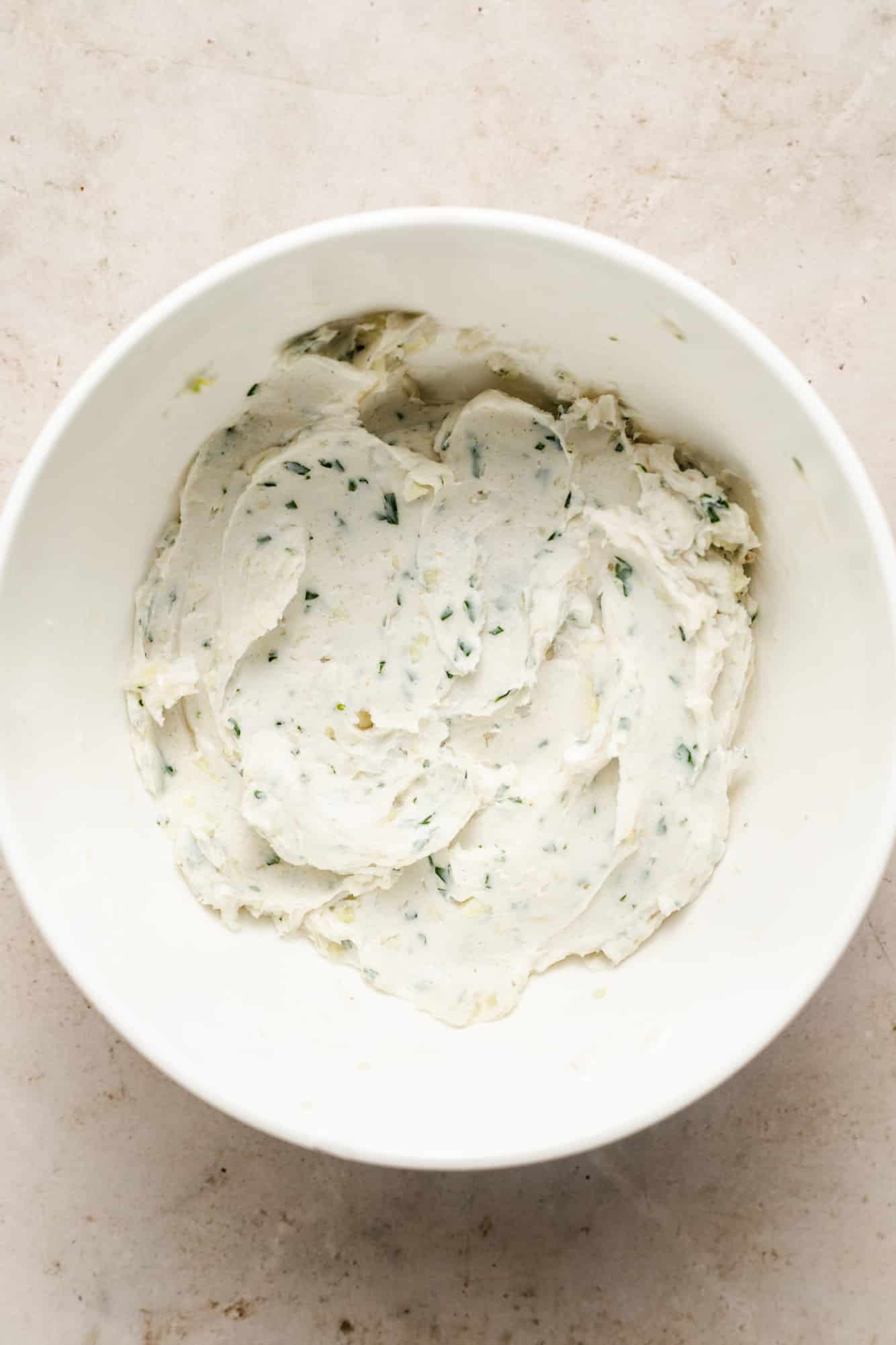 a vegan garlic butter spread with fresh herbs in a white bowl.
