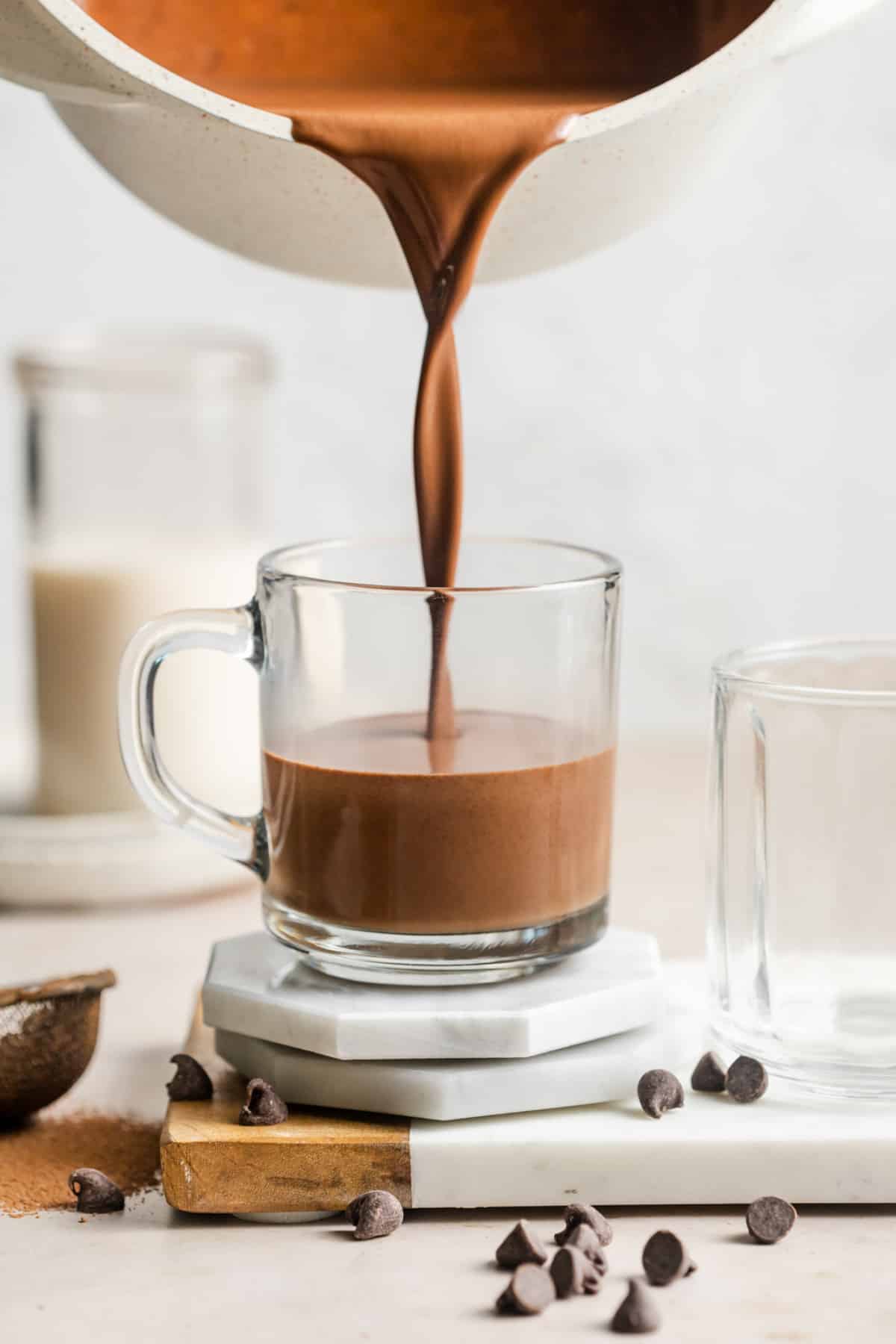 pouring vegan hot chocolate from a saucepan into a glass mug.