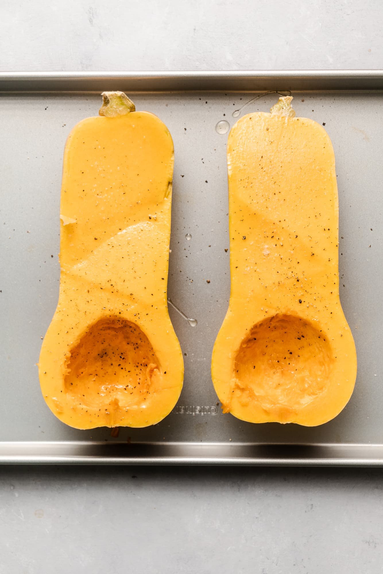 a butternut squash cut in half on a baking sheet.