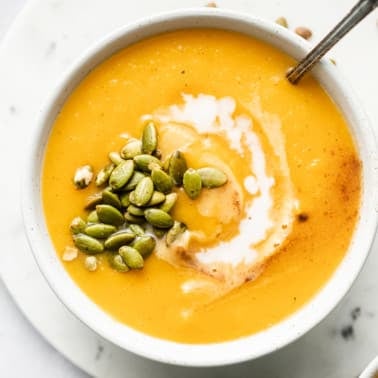 close up on butternut squash soup topped with coconut milk and pepitas in a white bowl.