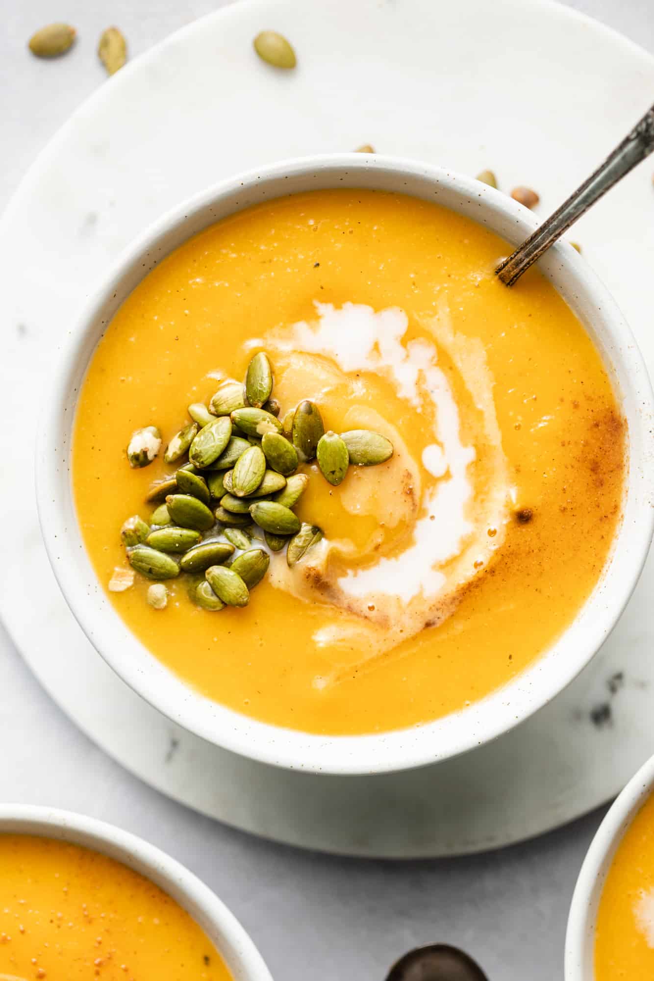 butternut squash soup topped with coconut milk and pepitas in a white bowl.