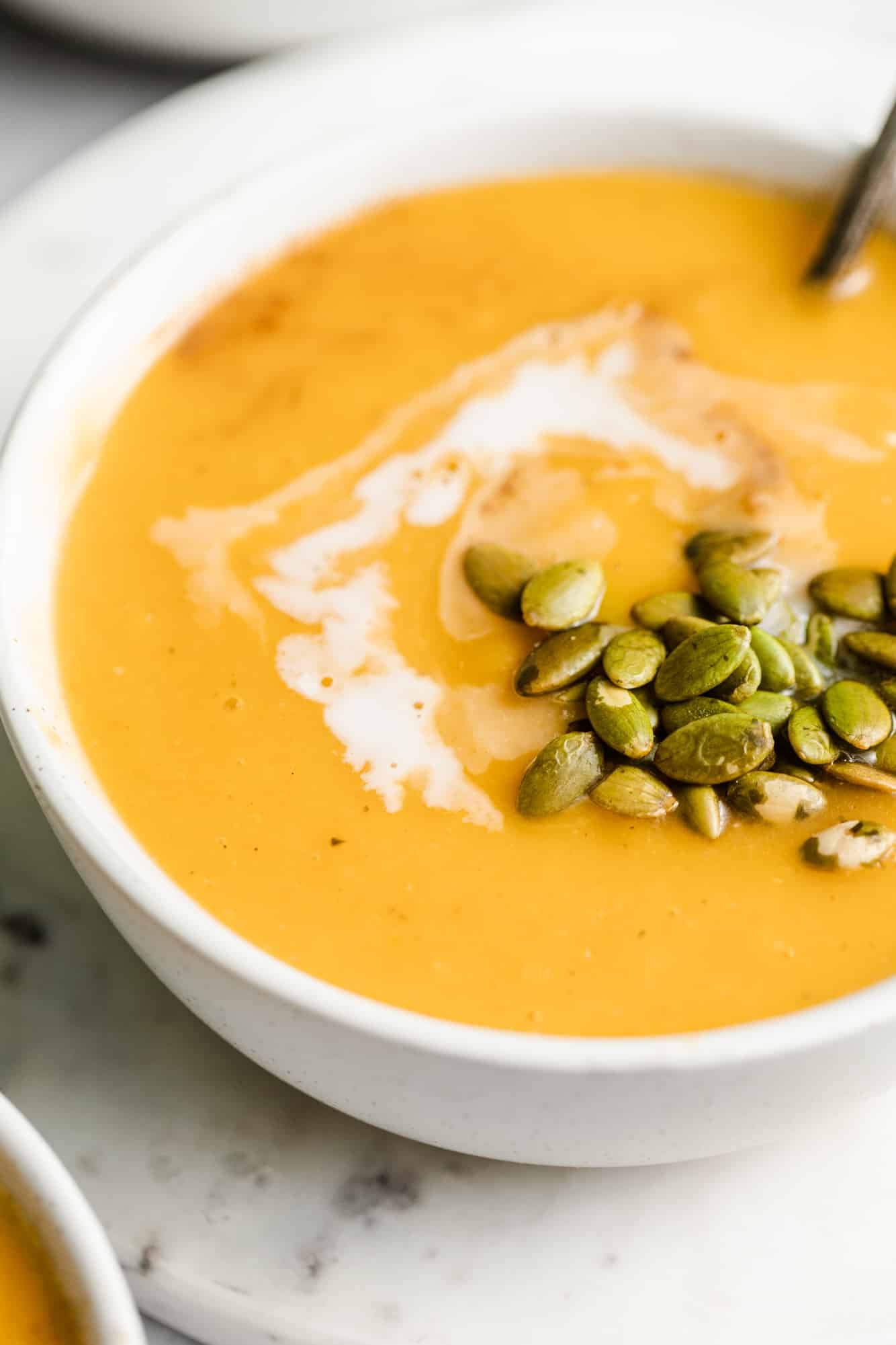 butternut squash soup topped with coconut milk and pepitas in a white bowl.