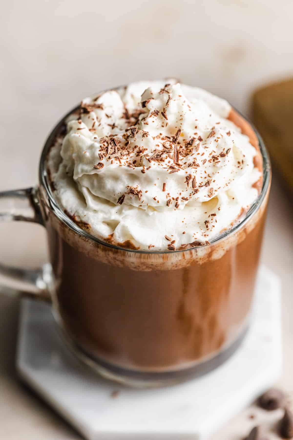 glass mug filled with hot chocolate and whipped cream on marble plate.