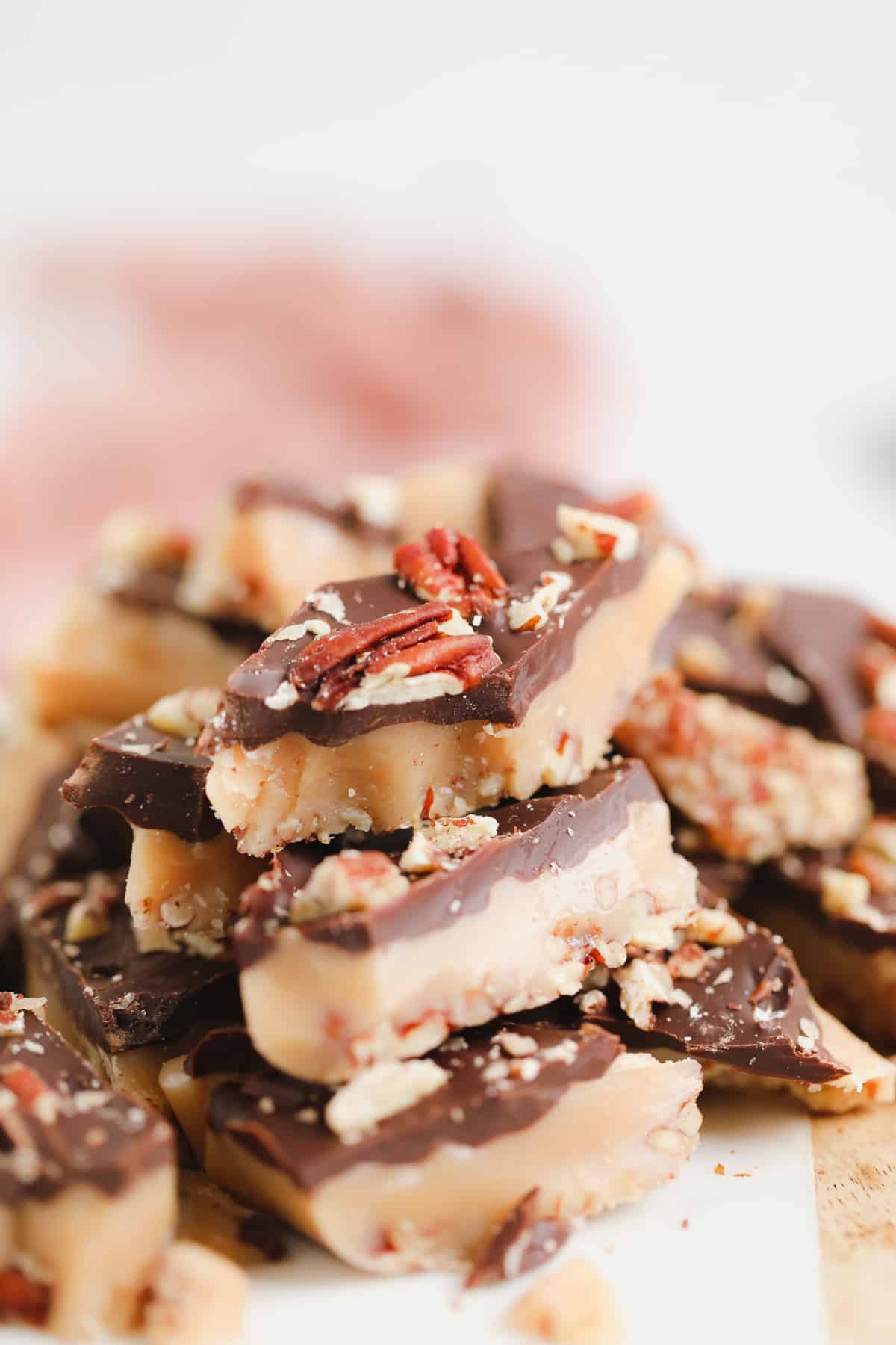 toffee with chocolate and pecans stacked up with a pink towel in background