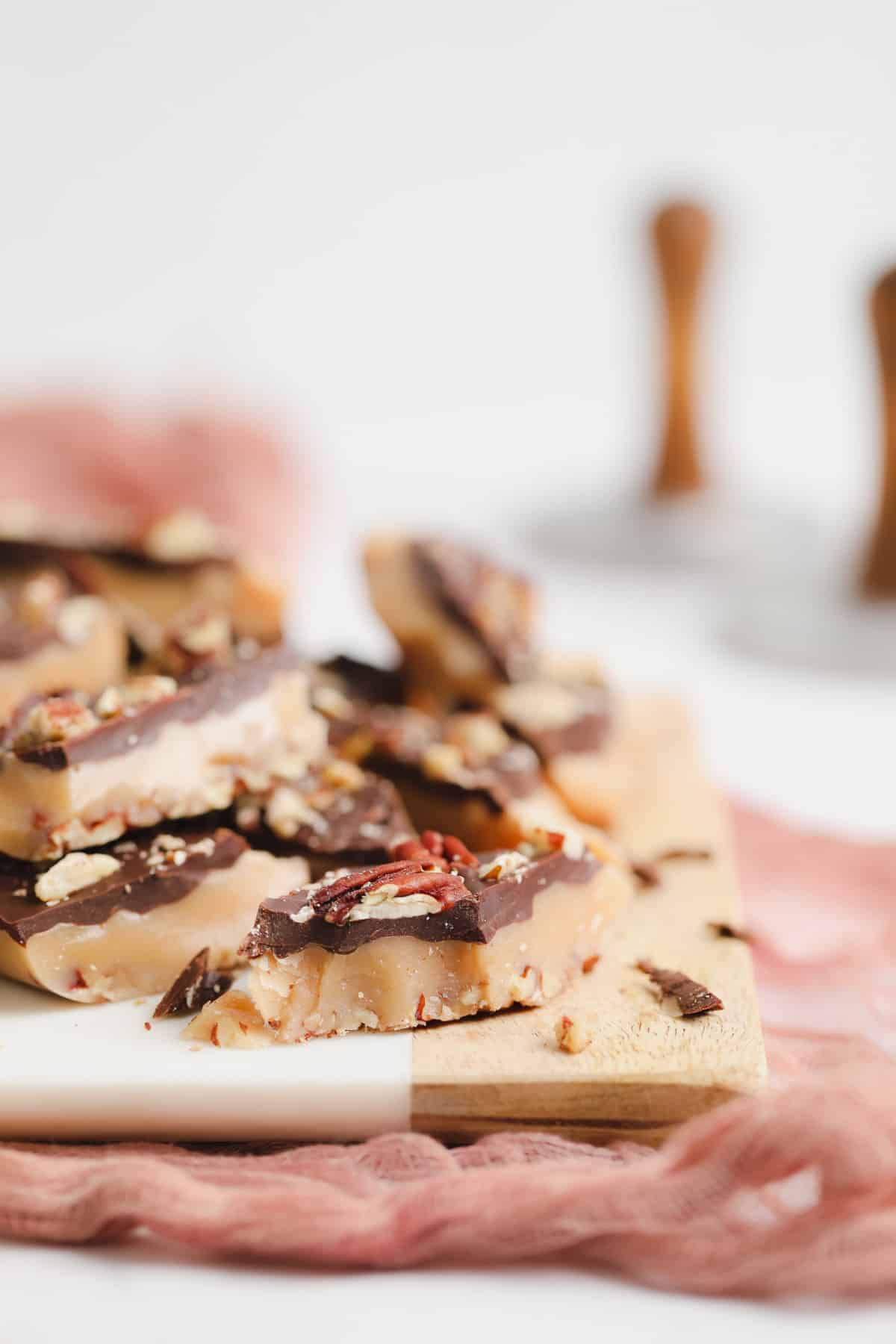 vegan toffee with chocolate and nuts on white and wood board.