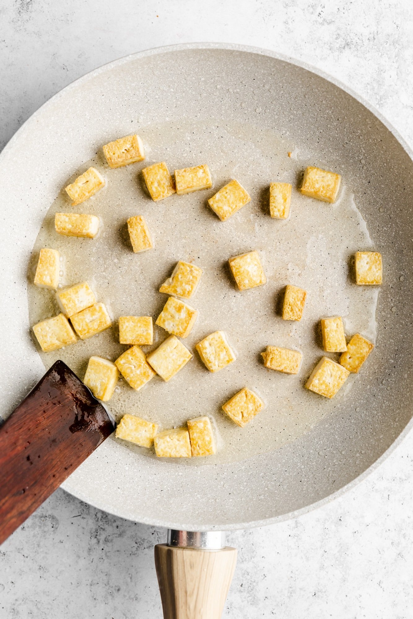 golden brown tofu cubes frying in a grey skillet.