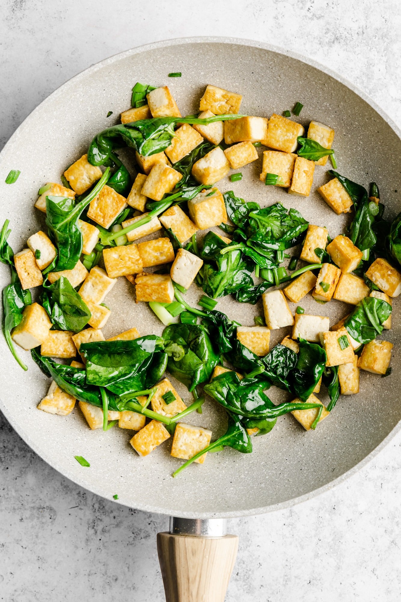 Tofu cubes and spinach stir-fried in a gray skillet.