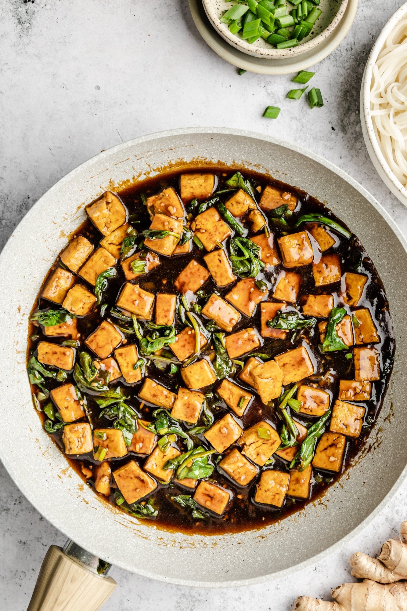 cooked tofu and spinach in a skillet with brown sauce.
