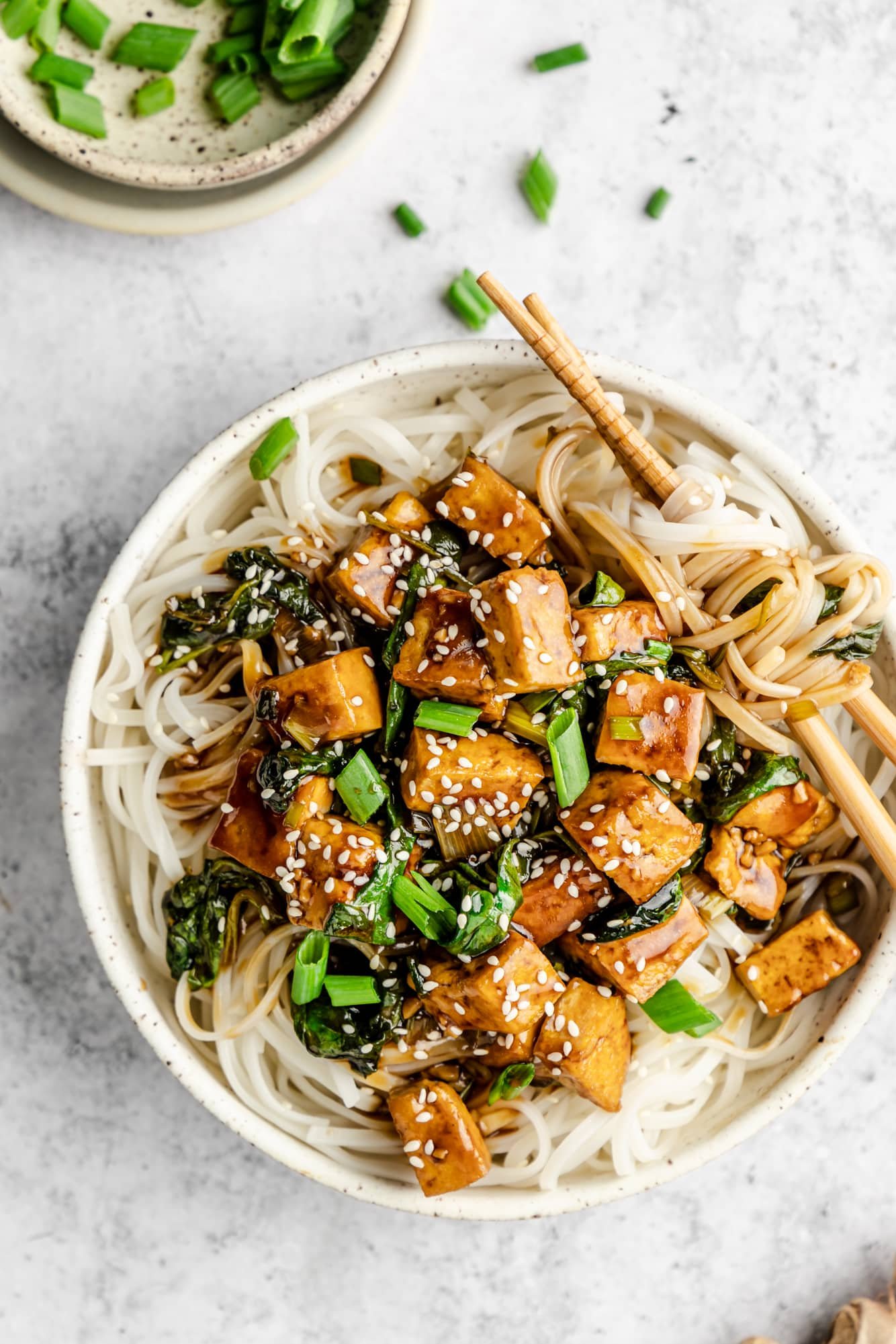 tofu stir fry served over rice noodles in a white bowl.