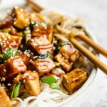 close up on tofu stir fry over rice noodles in a bowl with chop sticks.