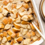 close up on a spoon taking a scoop of vegan bread pudding out of a white baking dish.