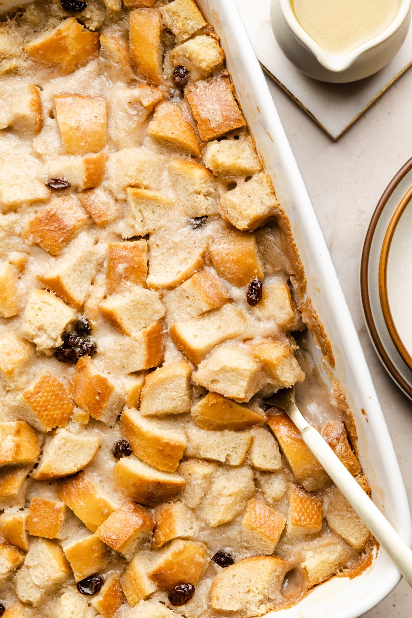 A spoon scooping vegan bread pudding from a white baking dish.