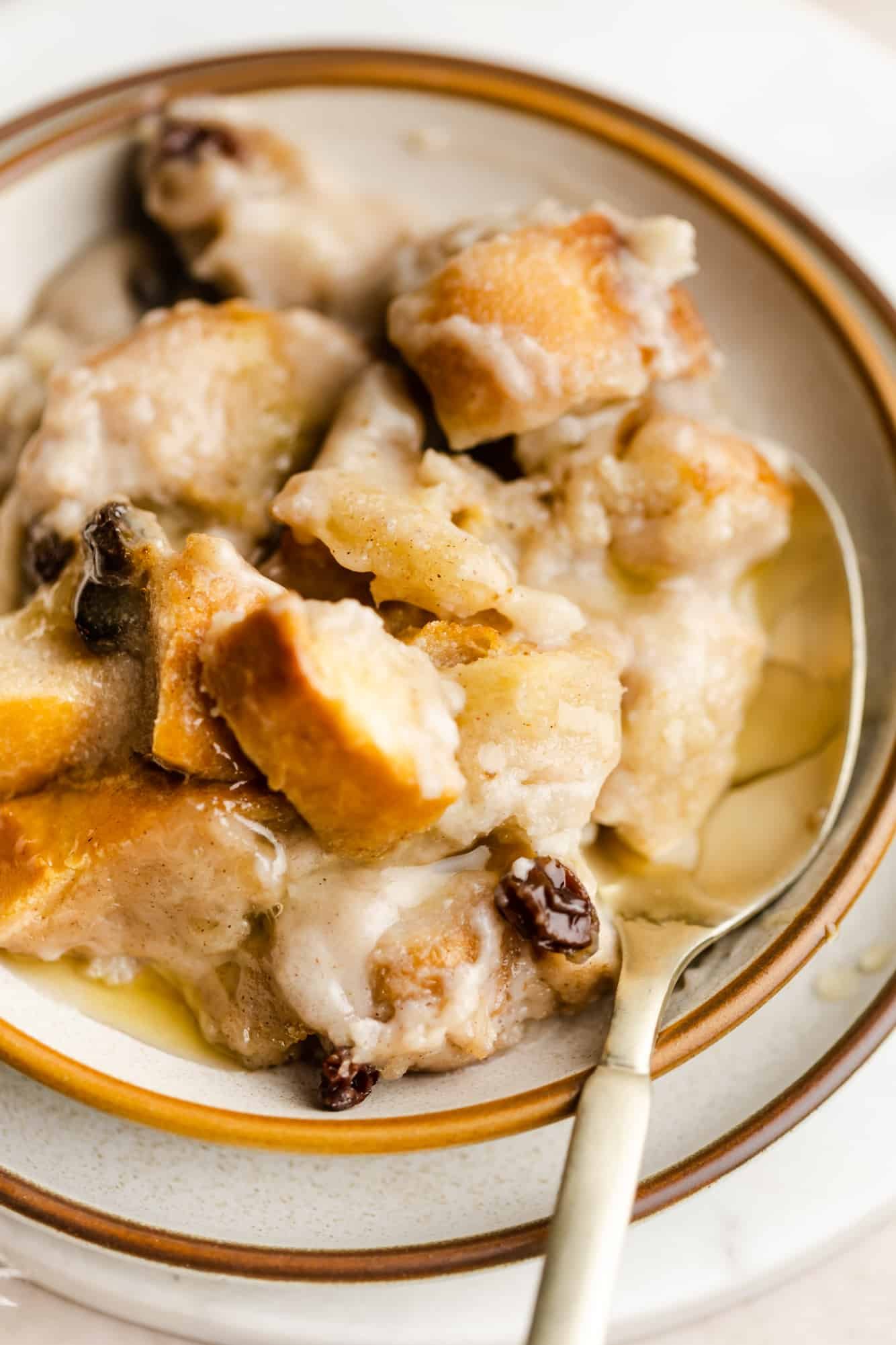 close up of a scoop of vegan bread pudding in a white bowl with a spoon.