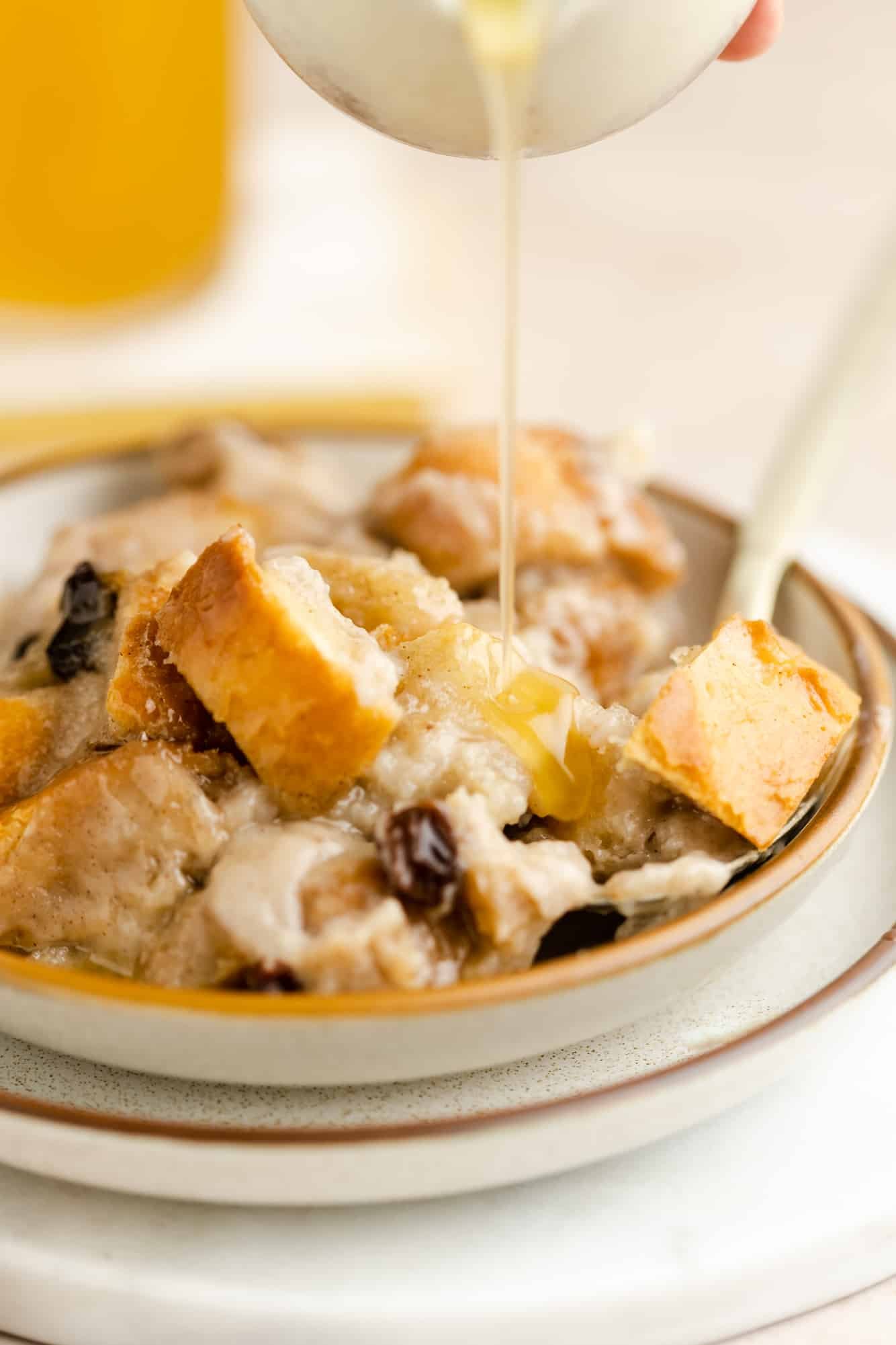 drizzling bourbon sauce over a scoop of vegan bread pudding in a bowl.