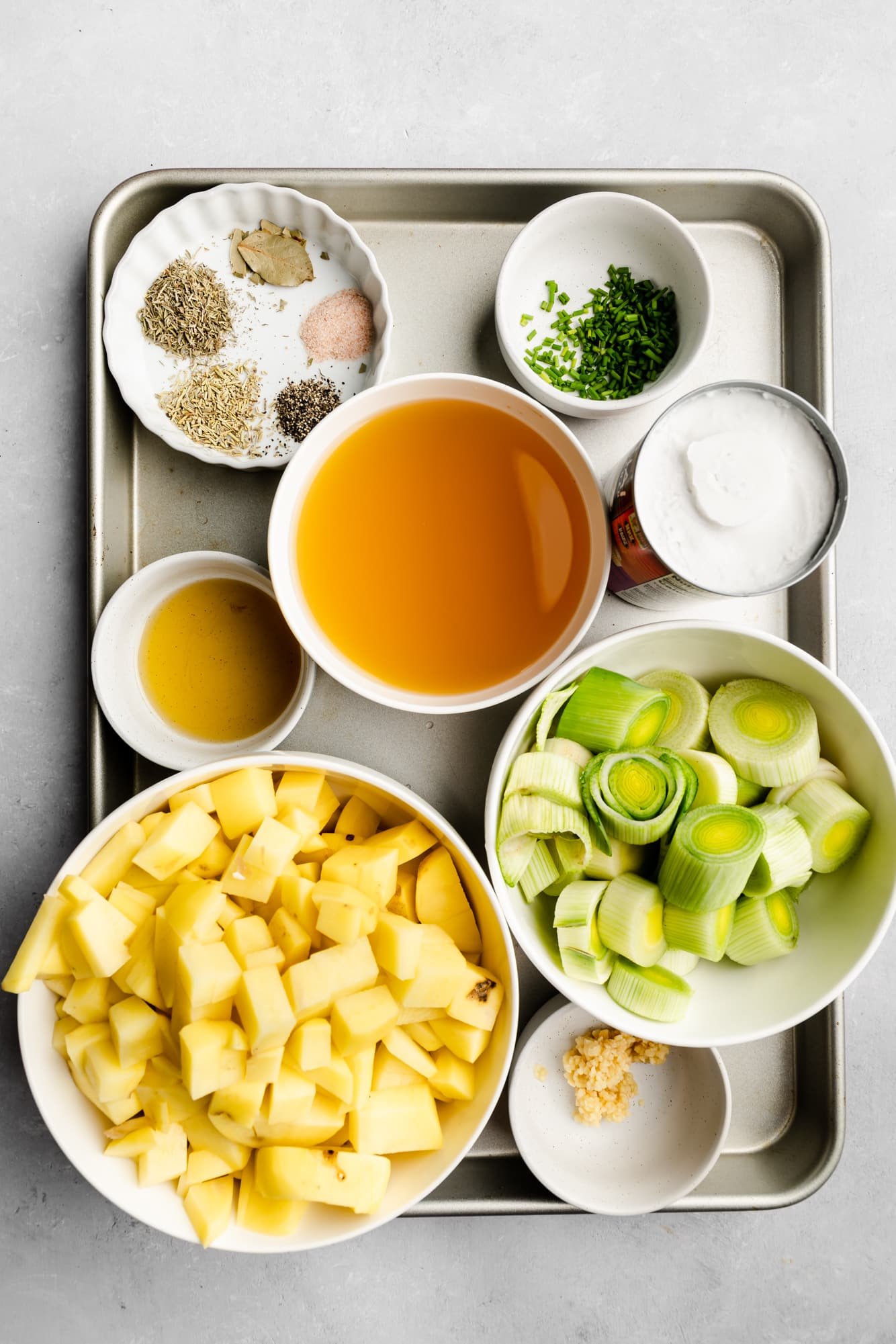 ingredients for Vegan Potato Leek Soup in individual white bowls on a metal tray.