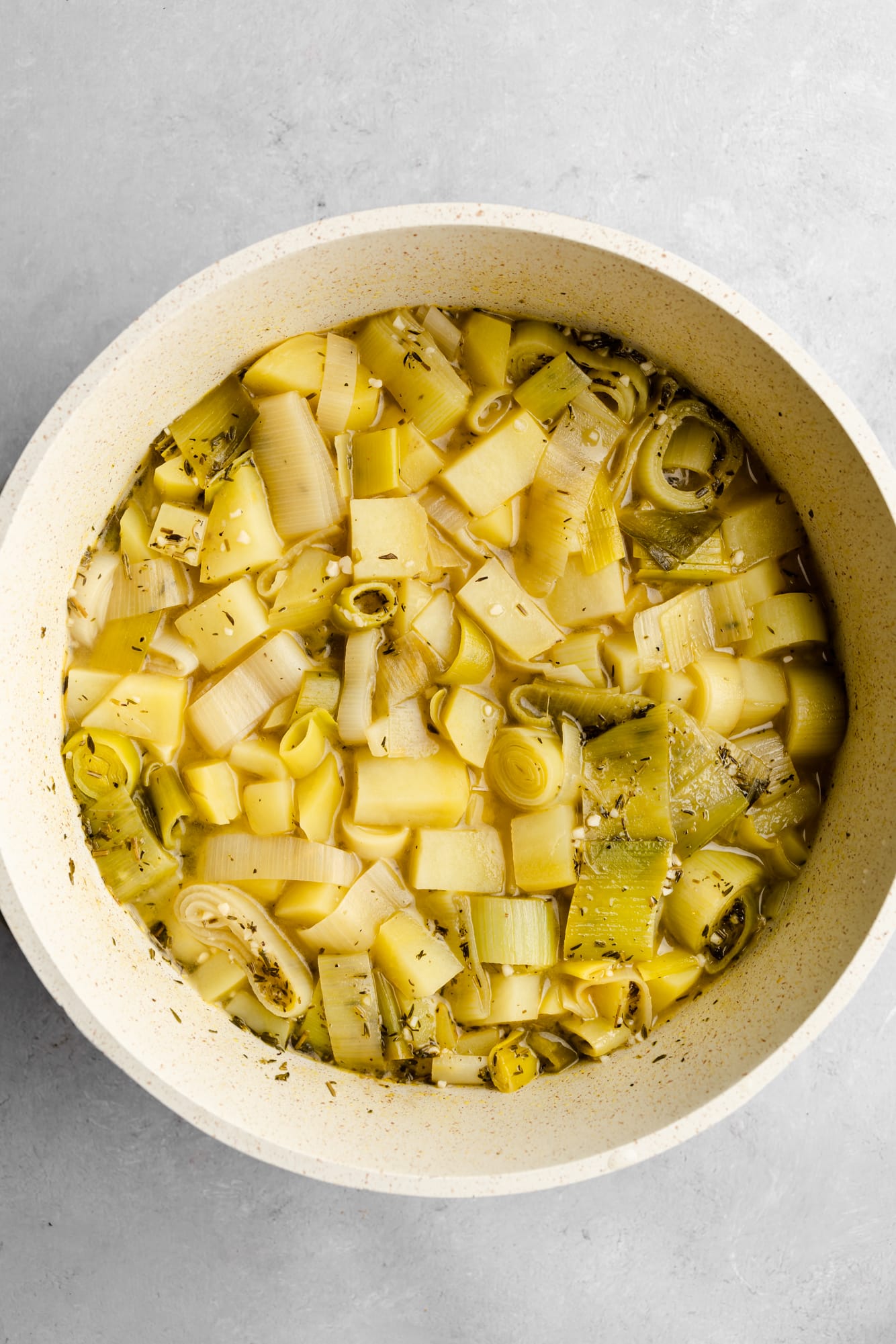 cooking vegan potato leek soup in a large white pot.