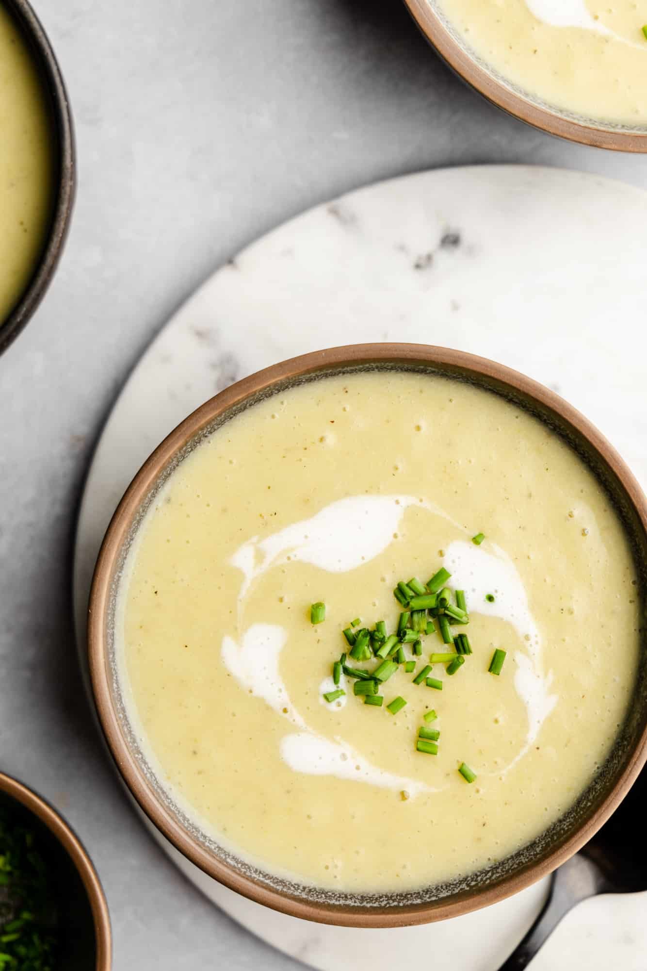 overhead view of a bowl of Vegan Potato Leek Soup topped with coconut cream and chives.