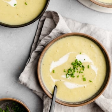 overhead view of a bowl of Vegan Potato Leek Soup topped with coconut cream and chives.
