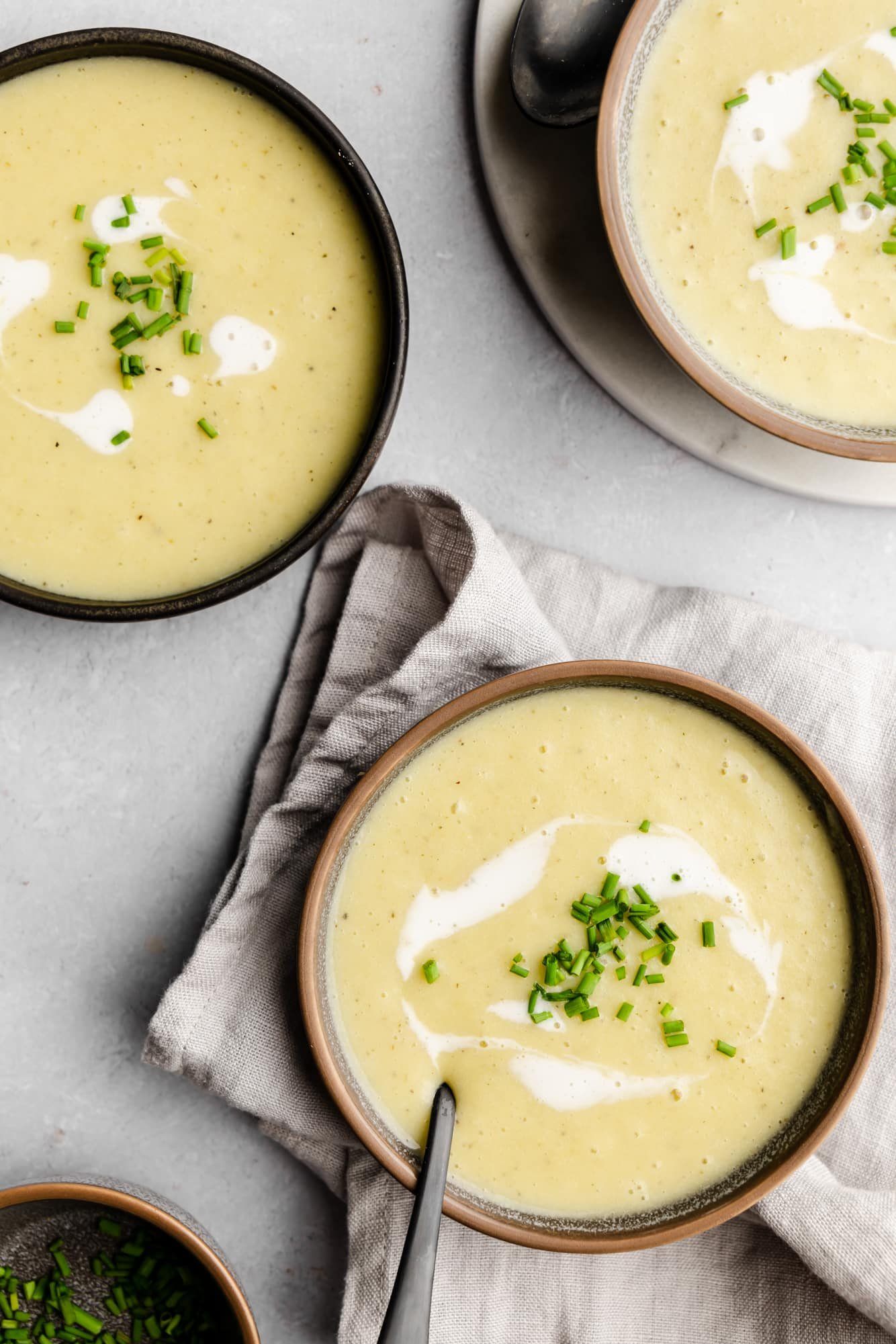 overhead view of 3 bowls of Vegan Potato Leek Soup topped with coconut cream and chives.