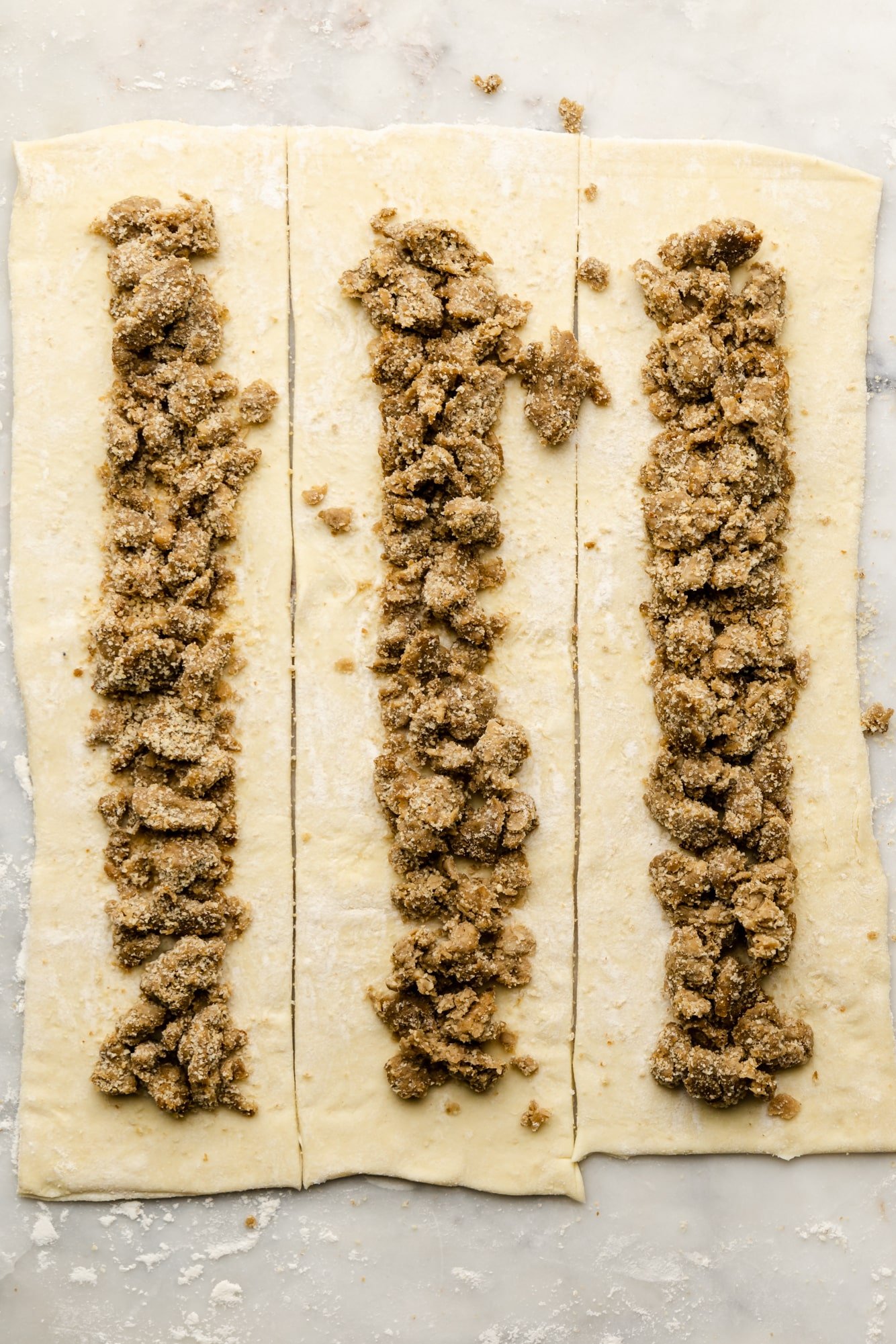 vegan sausage crumbles in rows on sheets of puff pastry.