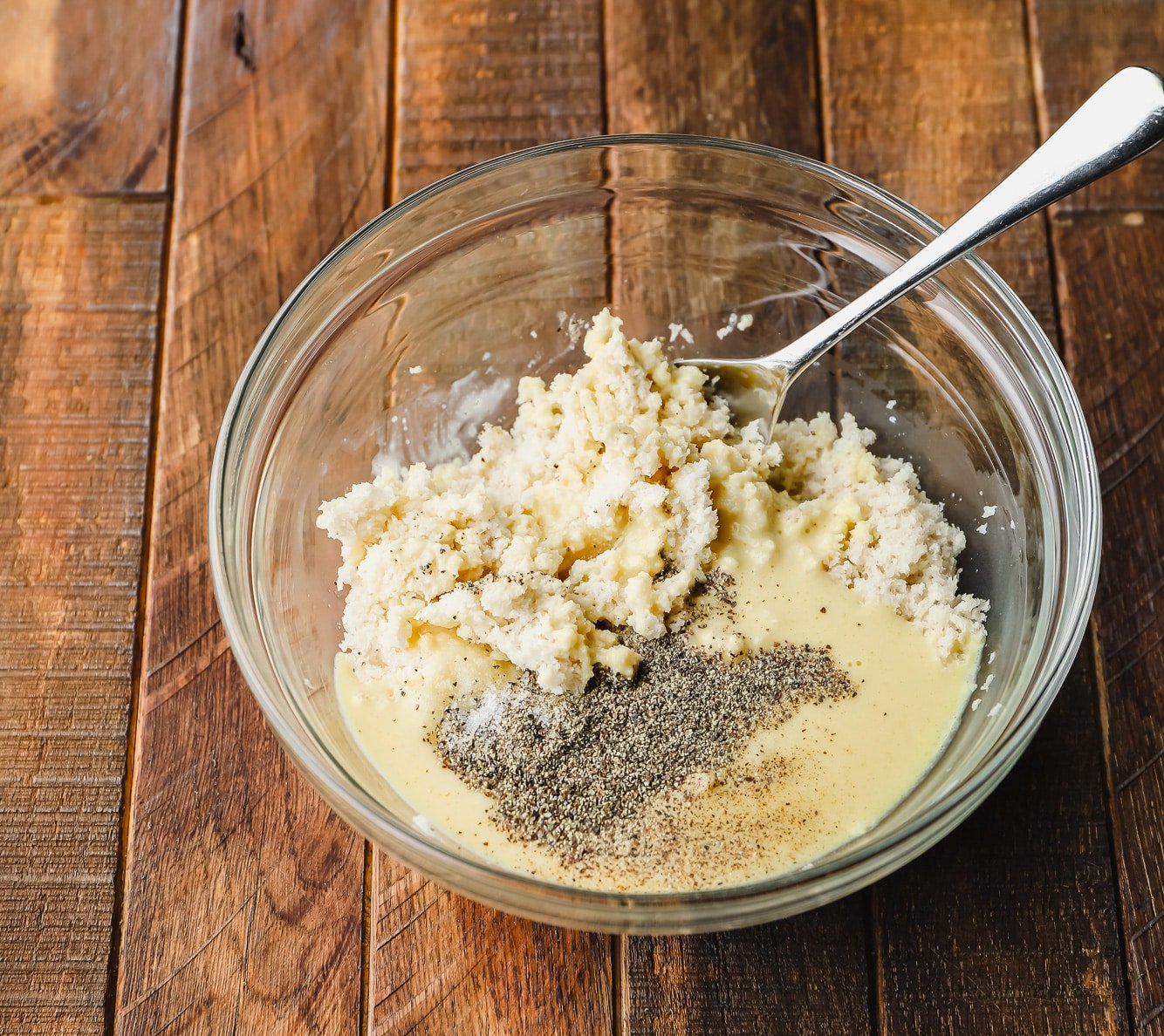 stirring breadcrumbs, liquid JUST Egg, and pepper together with a metal spoon in a glass bowl.