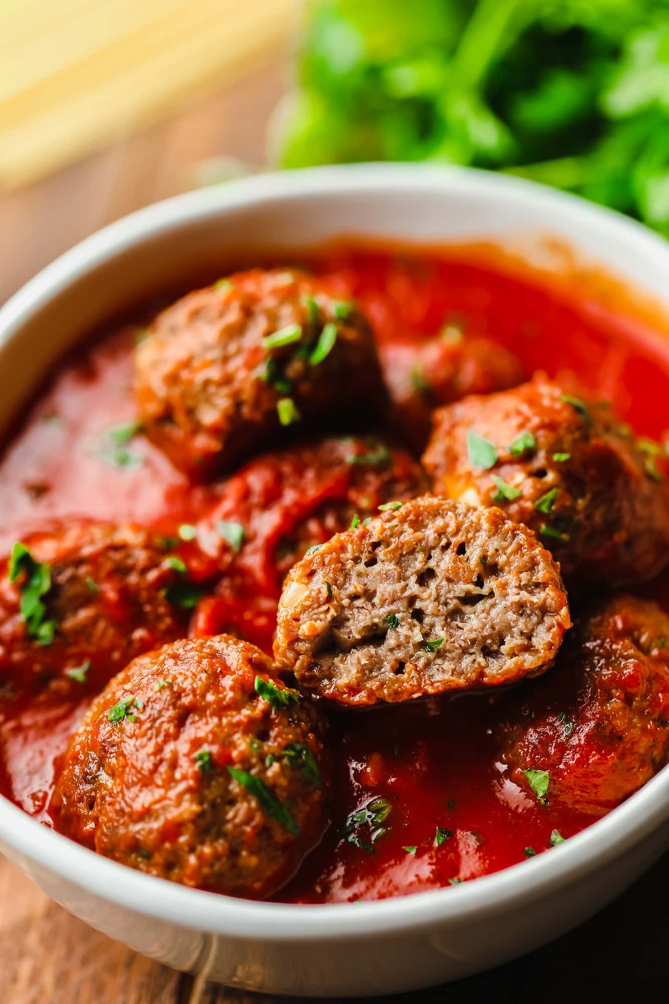 A vegan meatball cut in half on top of a pile of marinara sauce-covered vegan meatballs.