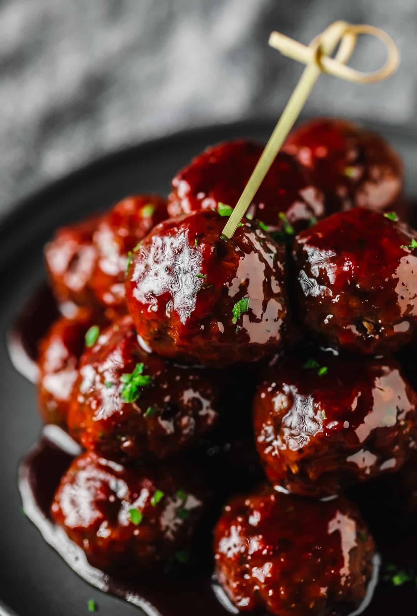 a pile of vegan grape jelly meatballs on a grey plate with a toothpick sticking out of the top.