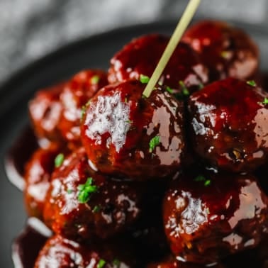a pile of vegan grape jelly meatballs on a grey plate with a toothpick sticking out of the top.
