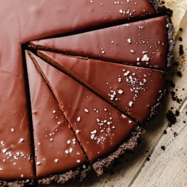 close up on a sliced vegan chocolate tart topped with flake salt.