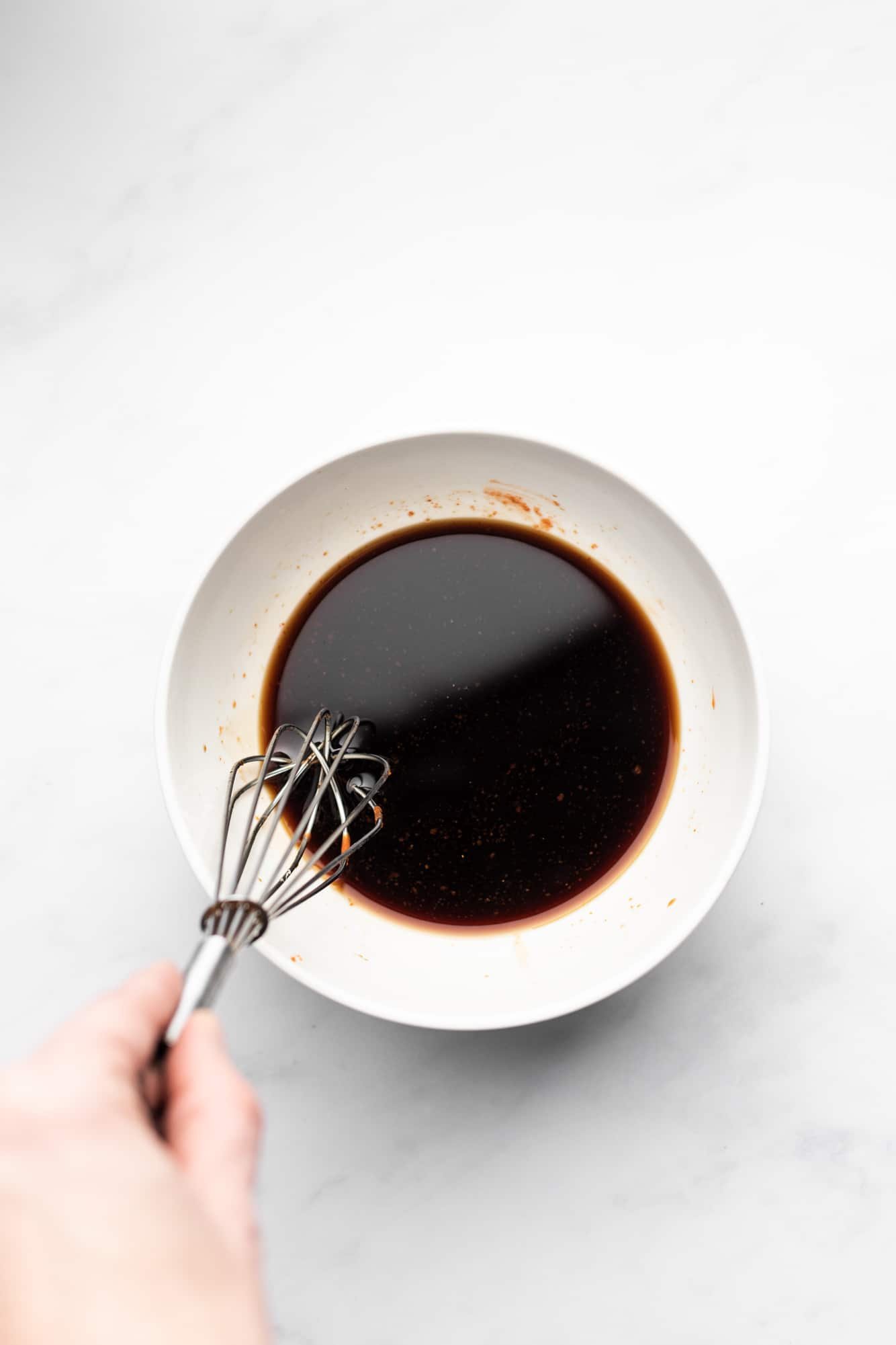 whisking a dark brown sauce in a white bowl.