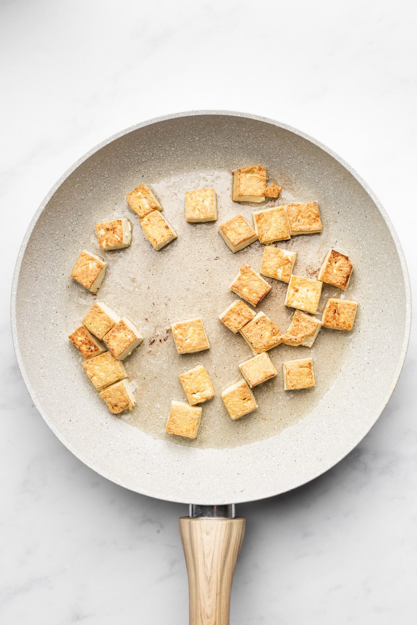 Fry cubed tofu pieces in a beige pan.