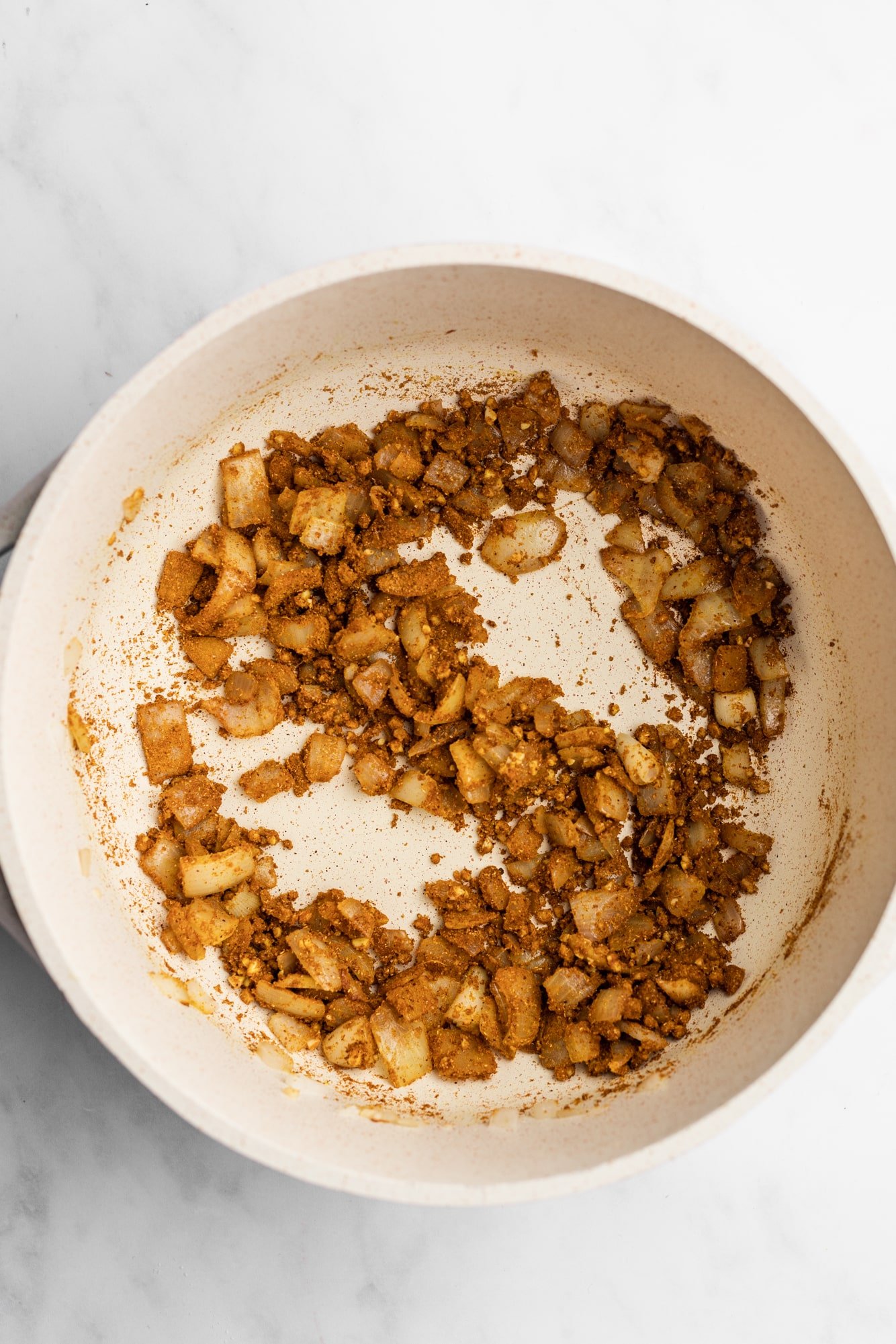 cooking spices onions and garlic in a large white pot.