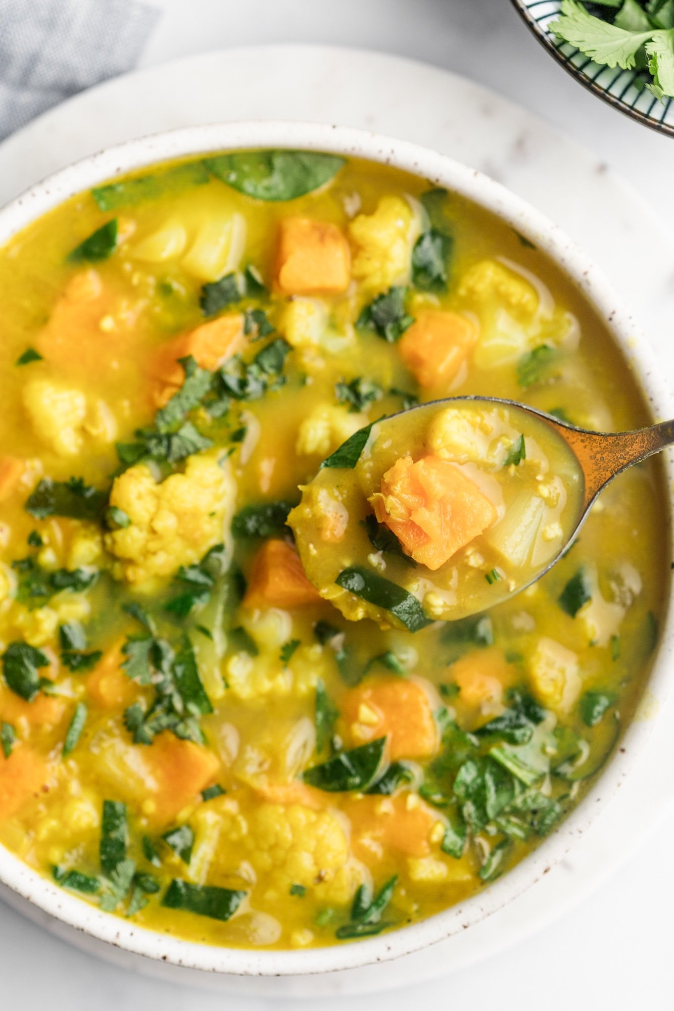 a spoon lifting a scoop of coconut curry lentil soup from a large white bowl.