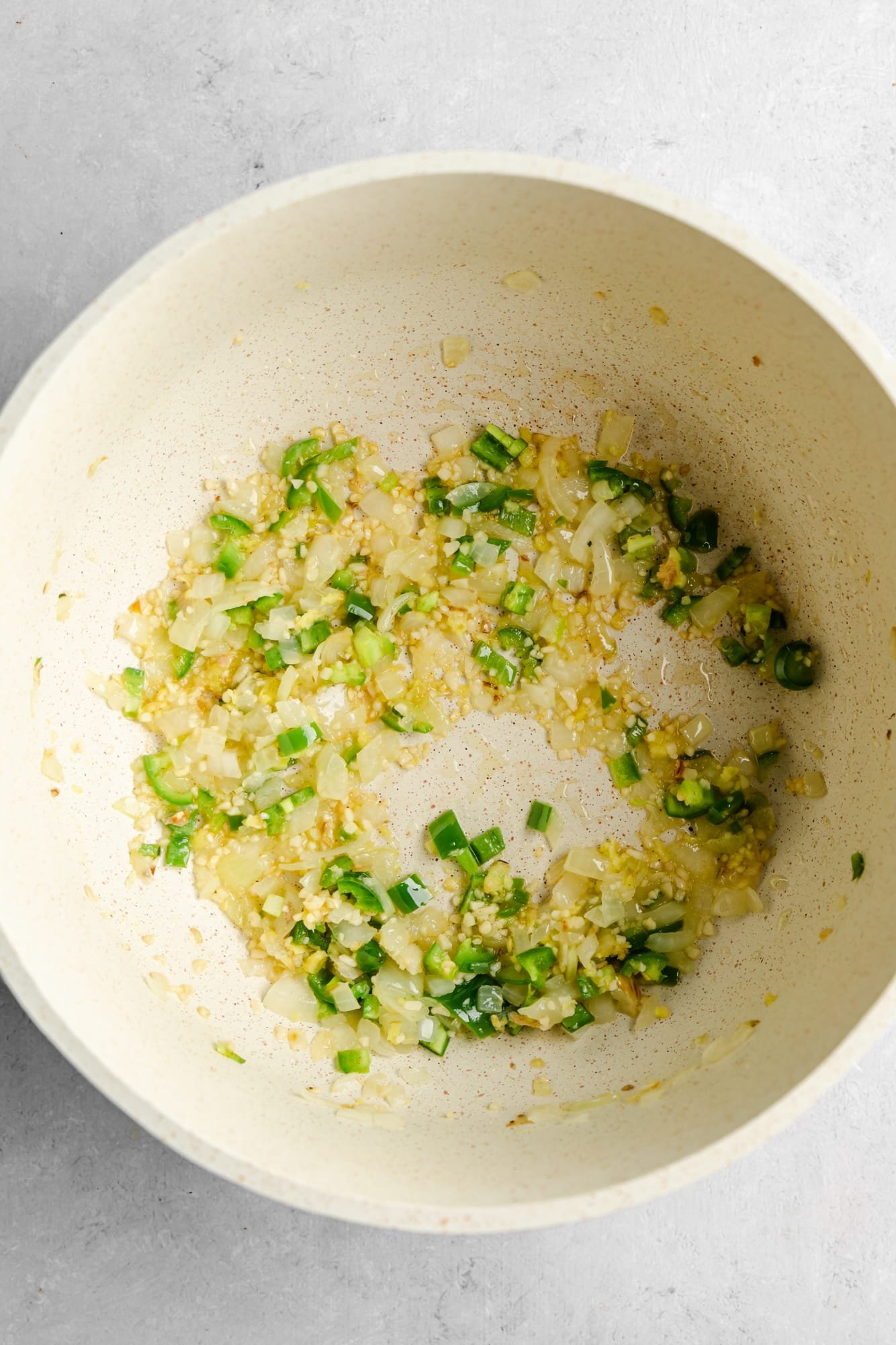 sauteeing onion, garlic, ginger, and green peppers in a large white pot.